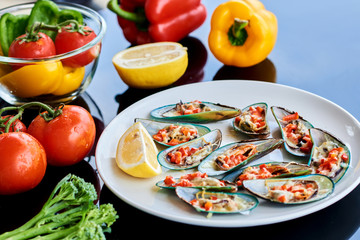 Fototapeta na wymiar Seafood. Shellfish. Baked mussels with parmesan cheese, tomato and lemon in shells on white plate. Plate of mussels, cold white wine, lemon and vegetables on the black background. Selective focus. .