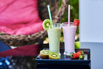 milkshake with fresh fruits in tall glass on garden table