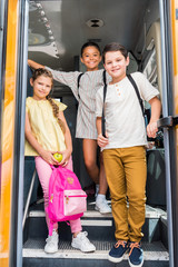 group of smiling schoolchildren standing at school bus