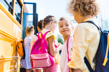 close-up shot of group of adorable schoolchildren standing near school bus