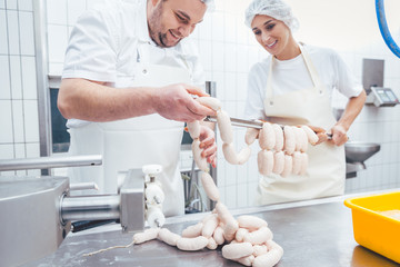 Team of butchers, woman and man, filling sausage in meat industry