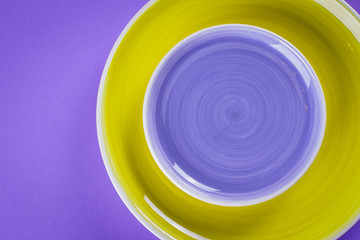 Colorful empty purple and yellow plates on purple background table. Top view, copy space