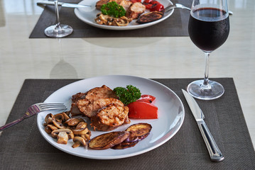 The served table with red wine and pork medallions  with vegetables at home.