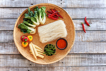 Asian food ingredients on old wooden background. Rice noodles, chili pepper, Chinese cabbage, green peppercorns, chili sauce, baby corn. Top view. Copy space.