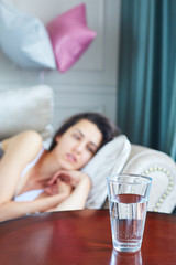 The girl lays on the couch after a party. A glass of water is located next to her on the table.