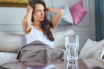 The girl is sitting on the couch after the party. A glass of water is located next to her on the table.