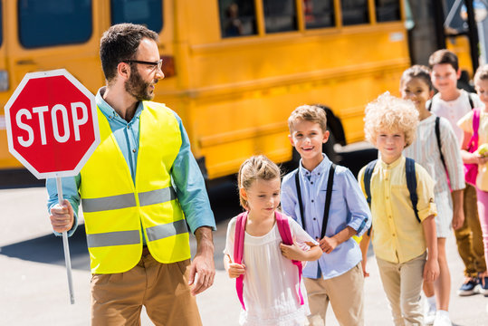 handsome traffic guard crossing road with pupils in front of school bus