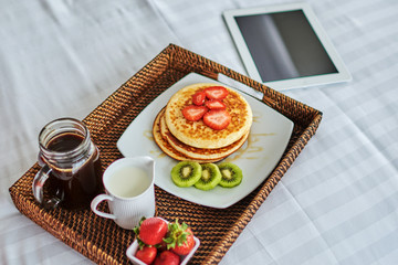 Breakfast tray in bed with tablet computer in hotel room. Business trip concept.