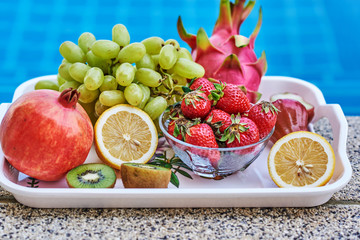 Tray of fruits next to a swimming pool.