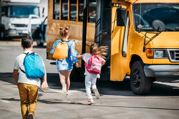 rear view of group of schoolchildren running to school bus