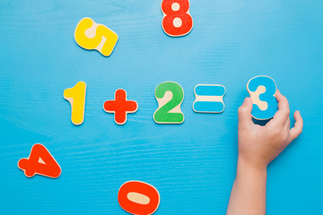Colorful learning numbers for little kids on the blue table. Girl's hand putting number three....