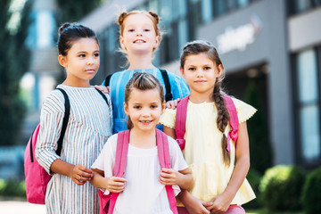 group of adorable schoolgirls with backpacks looking at camera