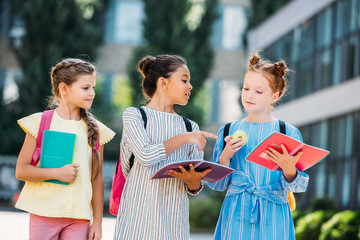 schoolgirls with notebooks spending time together after school and discussing homework