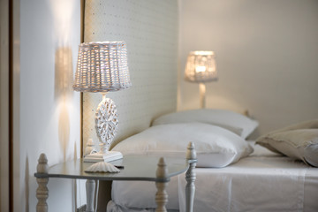 Lit up white bedroom lamps with beautiful ornaments standing on glass tables. Neutral colored modern bedroom with stylish interior design elements to set a warm and homely mood and atmosphere.