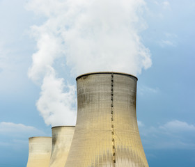 Three natural draft cooling towers of a nuclear power plant releasing clouds of water vapor against a dark stormy sky.
