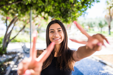 Portrait of a cheerful woman. Lovely woman showing victory or peace sign in the summer street