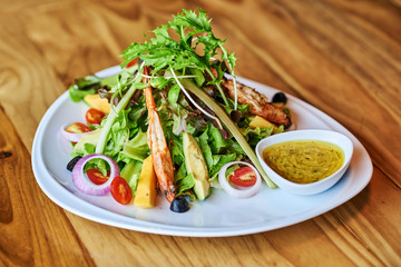 Salad with shrimps or prawn, tomato and arugula on wooden background.