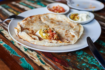 Homemade quesadilla with chicken, hand made salsa and yogurt on vintage wooden table.