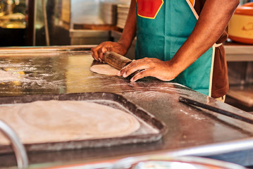 Men hands roll out dough close up. Asian men preparing dough for cooking local Indian Roti in the street market. Process to cooking most popular delicious snack. Street food vendor.