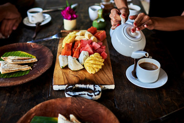Tropical breakfast with coffee and fresh tropical fruits on old wooden board.