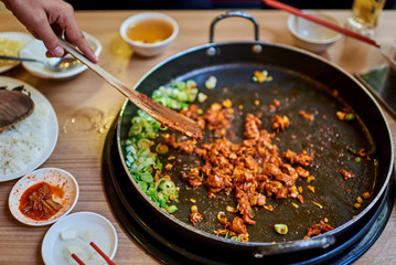 Korean spicy Kimchi bbq pork served on a hot pan with side dishes and rice as a background..