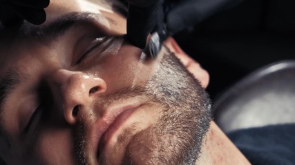 Close up of a handsome man getting his beard shaved in a hairdresser professional hairdresser using a razor shaving his customer profession.