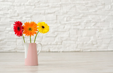 .Bouquet from three gerbera in a vase on the floor on a background of a white brick wall..
