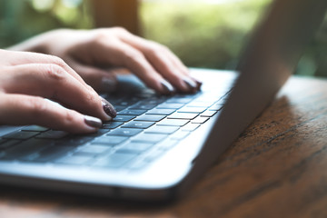 Closeup image of woman's hands working and typing on laptop keyboard on wooden table with green nature background