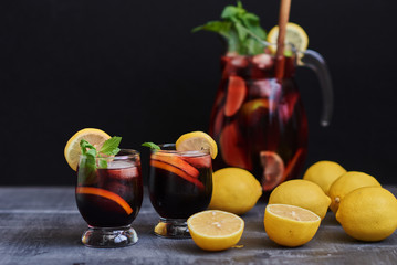Fruit drinks with ice cubes. A pitcher of sangria accompanied by a glass on a black table. Selective focus.