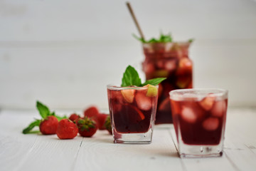 Cold sangria in a glass on white background. Summer cold drinks: homemade  sangria with ice cubes, and mint in glass on wooden background. Sangria with slices of fruit and ice, selective focus.