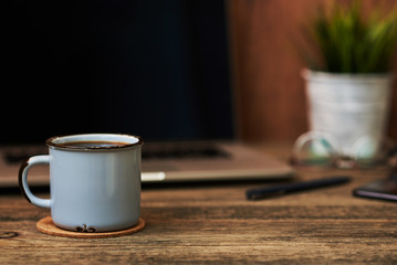 Workplace with close up cup of coffee, office supplies and laptop in the background. The blank screen can be used to put some text or images. Business concept with copy space. Vintage style..