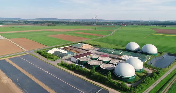 Plant for the production of biogas in the green field, plant for the production of biogas against the background of wind generators view from above