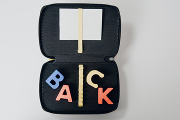 Opened yellow pencil case with the words "back" arranged in wooden letters. The concept of returning to school, education. The children are going back to school.