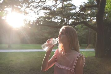 Beautiful young girl drinking water from a plastic bottle after a long walk in the woods