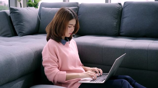 Beautiful young smiling asian woman working on laptop while enjoying drinking coffee in living room at home. Happy female buying online shopping at home. Lifestyle woman at home concept.