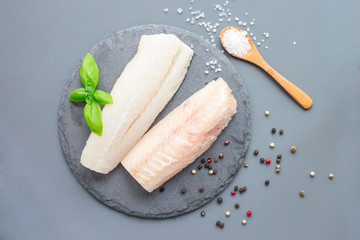 Fresh raw cod fillet with spices, pepper, salt, basil on stone plate, horizontal, copy space, top...
