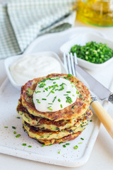 Vegetarian zucchini fritters or pancakes, served with greek yogurt and green onion on ceramic plate, vertical