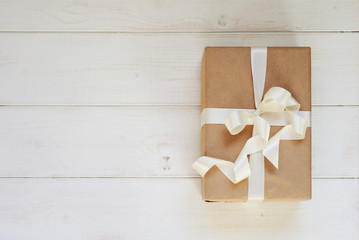 Craft paper  handmade gift box with shiny white satin ribbon  on light wooden rustic background. Presents with ribbon for christmas, valentine's day, birthday or new year for any holiday concept.