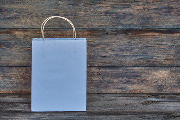 Mock-up of white craft paper package with handles, empty shopping bag with area for your logo or design, wooden board in the background, food delivery, sale, consumerism and advertising concept.
