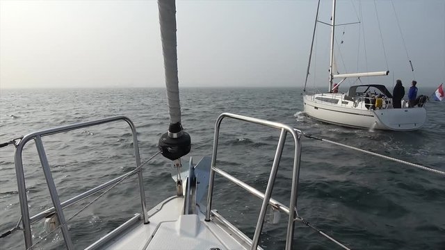 Footage taken from modern sailboat bow showing second boat passing at starboard both vessels moving to open sea and propelled by combustion engine the sails still folded 4k high resolution quality