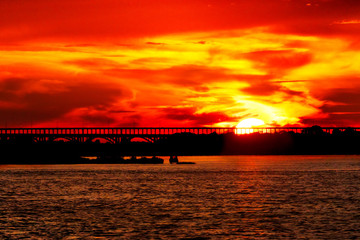Red sunset with red sun and silhouette of bridge on far