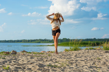 Beautiful happy young woman in a hat and in shorts running along the seashore