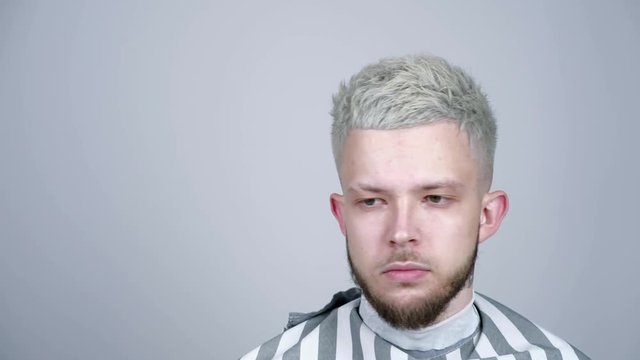 Blond young man looking to the side stroking his beard.