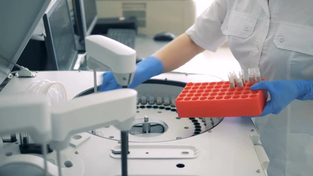 Test tubes are getting inserted into a biochemical analyzer by a lab worker