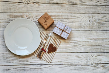 Vintage or rustic christmas table setting from above. Elegant empty white plate, cutlery on linen napkin on rustic planked wood - country style.