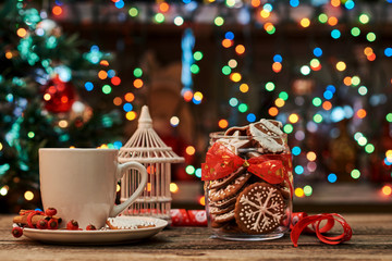 Cup of coffee with gingerbread and Christmas decorations on a background of bright lights