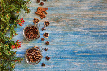 Christmas wooden background  fir branches and berries. Glass jars with anise and  dried lemon. Christmas Spices.