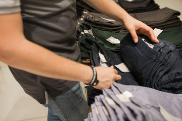 A young man in a gray T-shirt chooses clothes in a shopping mall.