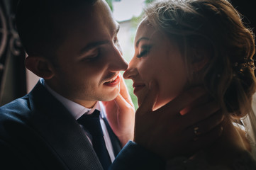 A beautiful bride and a stylish groom stand and hug in the back light. Wedding concept. Wedding portrait of cute and smiling newlyweds.