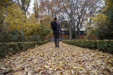 Young man walking by fallen leaves on the ground in a park a cloudy day